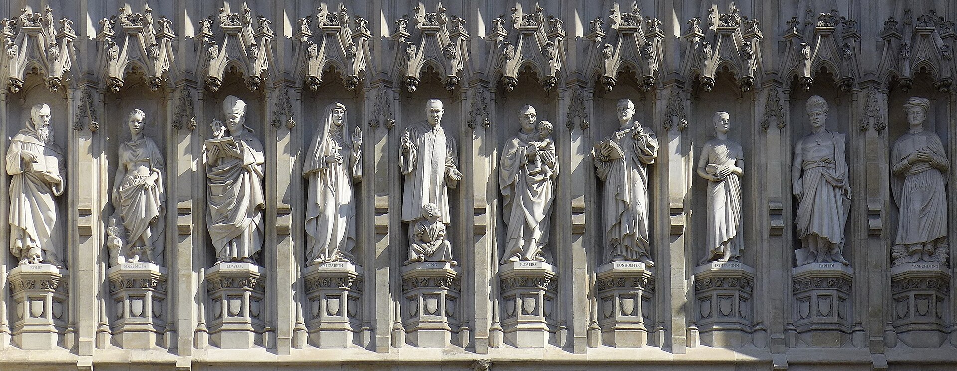 A row of ten carved stone statues in niches above a Gothic church doorway