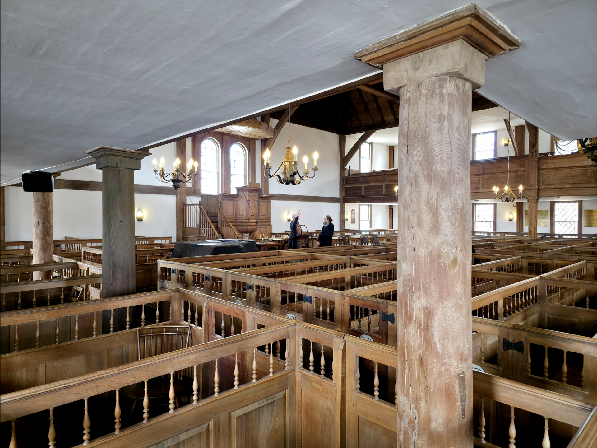 Interior of a wooden meetinghouse with a high pulpit, rows of enclosed box pews, a gallery on three sides and exposed curved roof timbers overhead