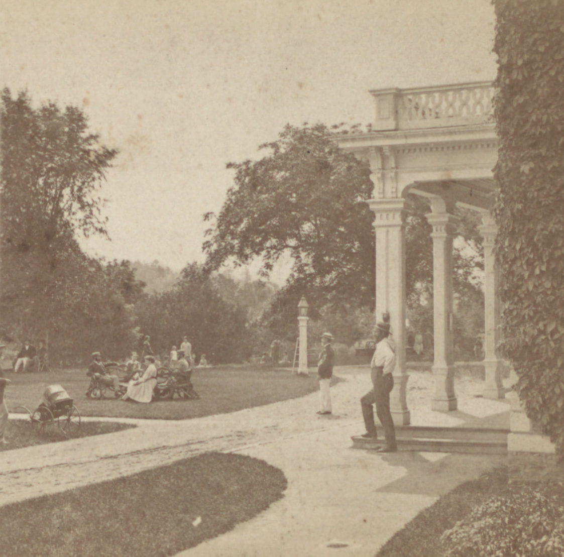 Photograph of a large brick building with a columned portico and tall windows, facing a broad lawn with trees