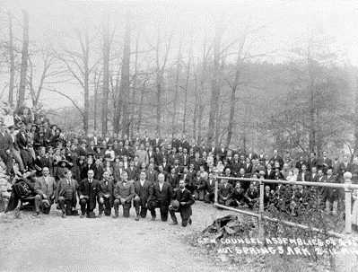 Black and white group photograph of about three hundred men and women standing in rows in front of a building, with a row of men kneeling at the front