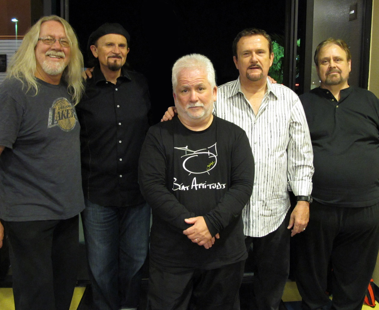 Five men, most with gray or white hair, standing close together indoors and smiling for a group photograph