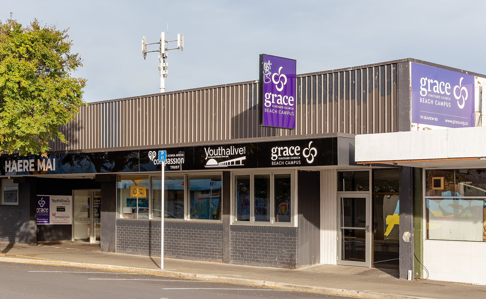 A single-story storefront on a street with purple signs reading grace Vineyard Church Beach Campus, next to signs for Youthalive and Compassion Trust.