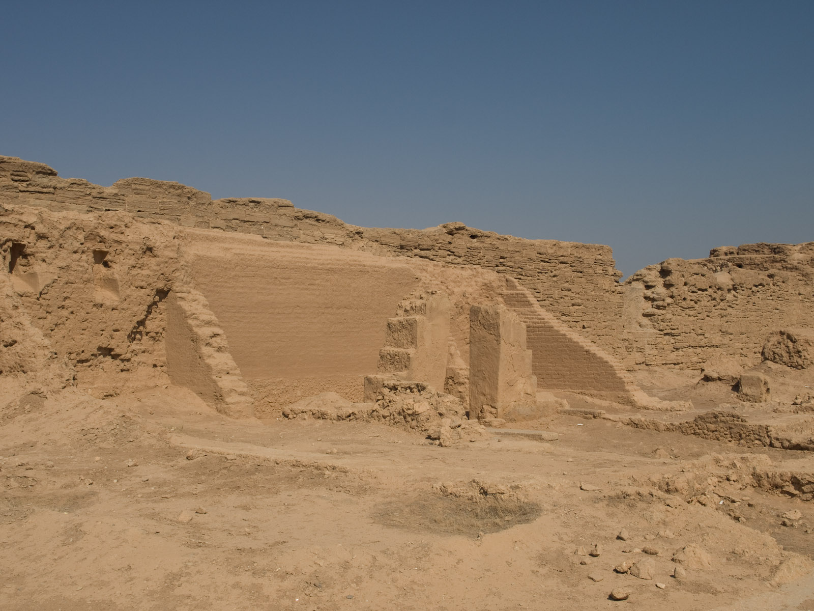 Low mud-brick walls of an excavated ancient house with a doorway, on a sandy site in the desert