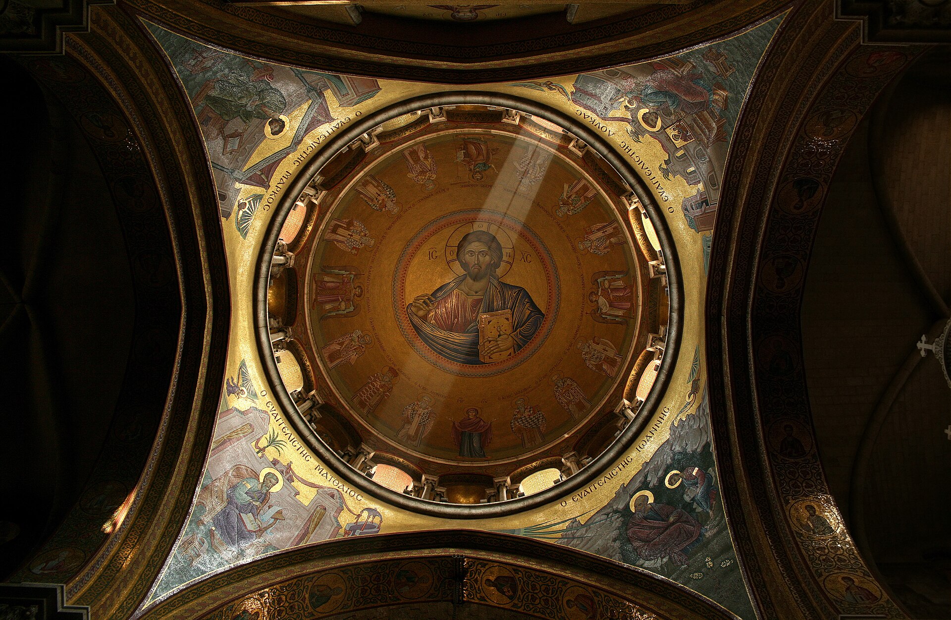 Interior of a large church with a high arch, a gilded iconostasis screen, hanging lamps and a dome above