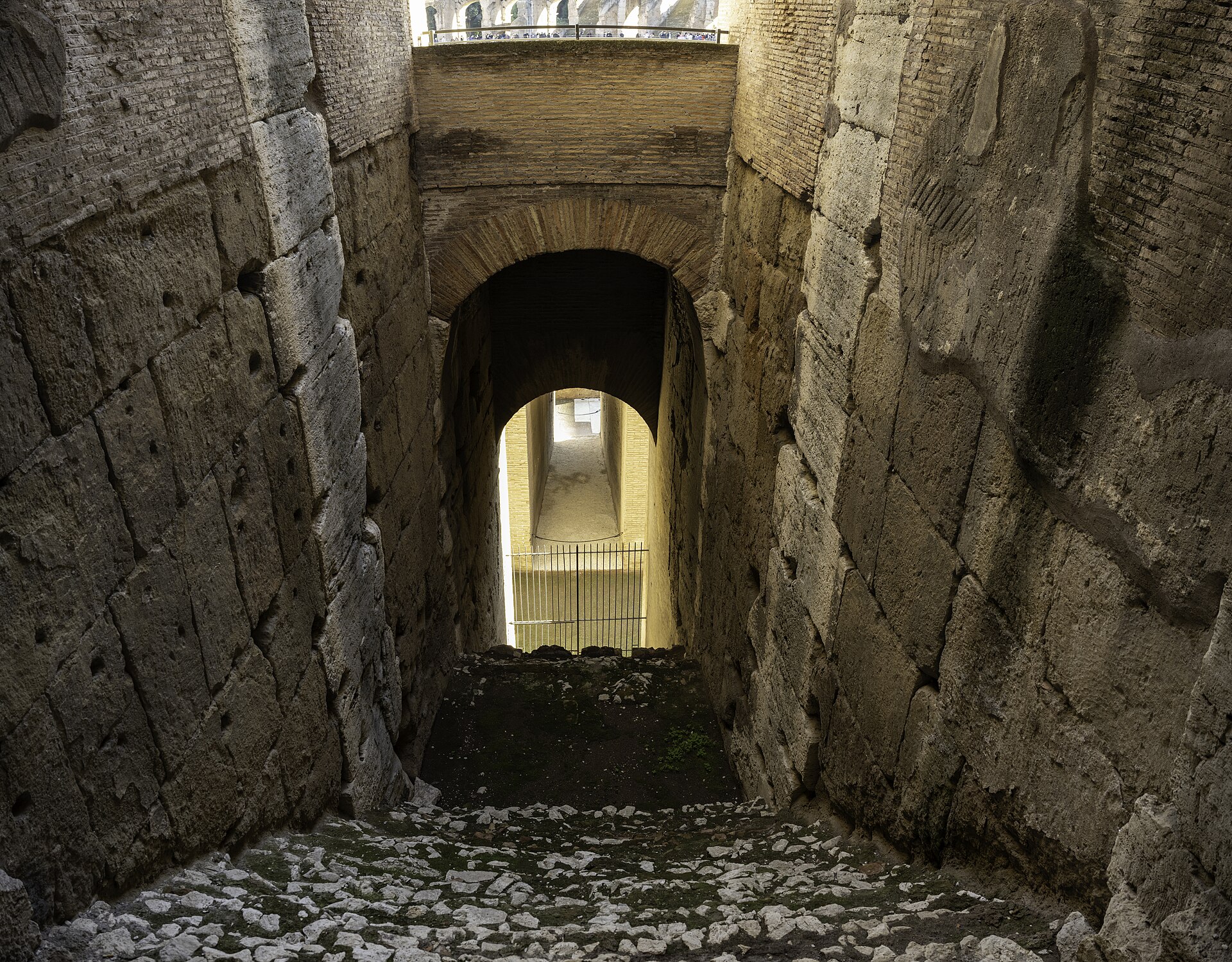 The Colosseum in Rome in daylight, its curved outer wall of stone arches standing in four stories, with the broken upper section on one side