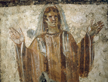 A faded wall painting of a woman in a long robe standing with both arms raised and hands open in prayer