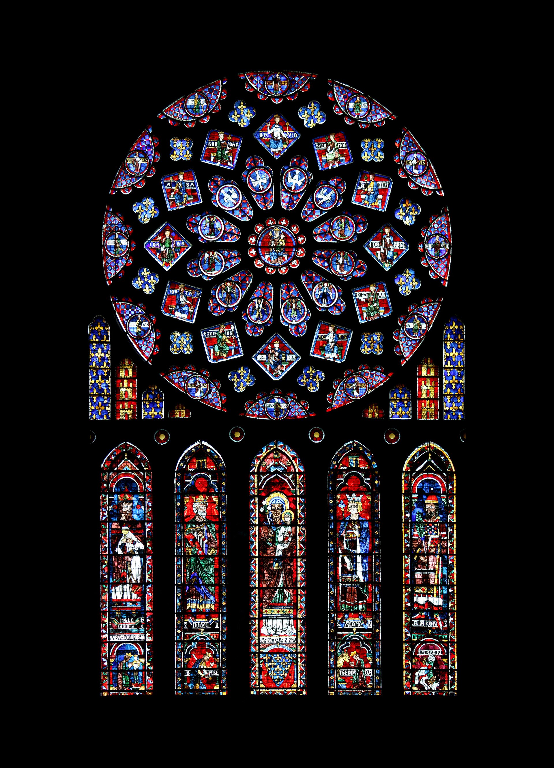 A circular stained glass window with a central medallion surrounded by rings of small square and diamond shaped panes in deep blue and red