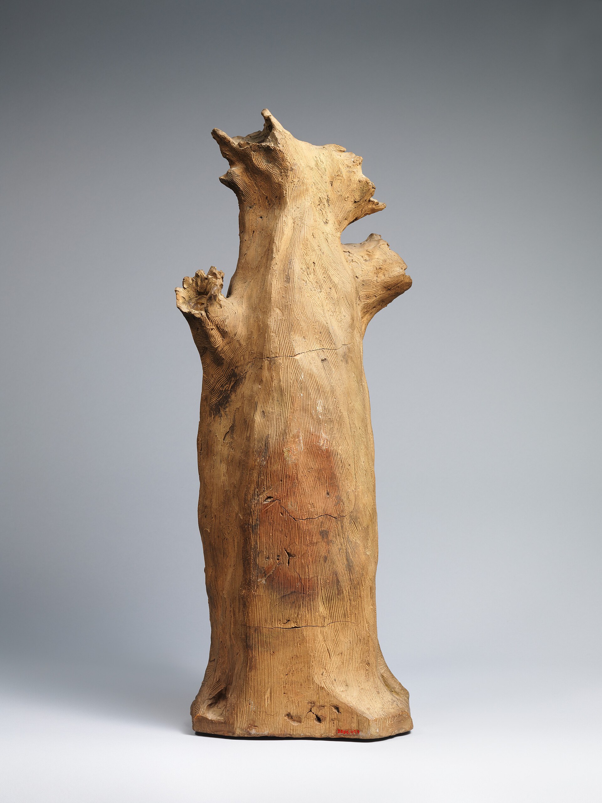 A small terracotta sculpture of a kneeling crowned man in a long robe with bare feet, hands raised, before a closed gateway