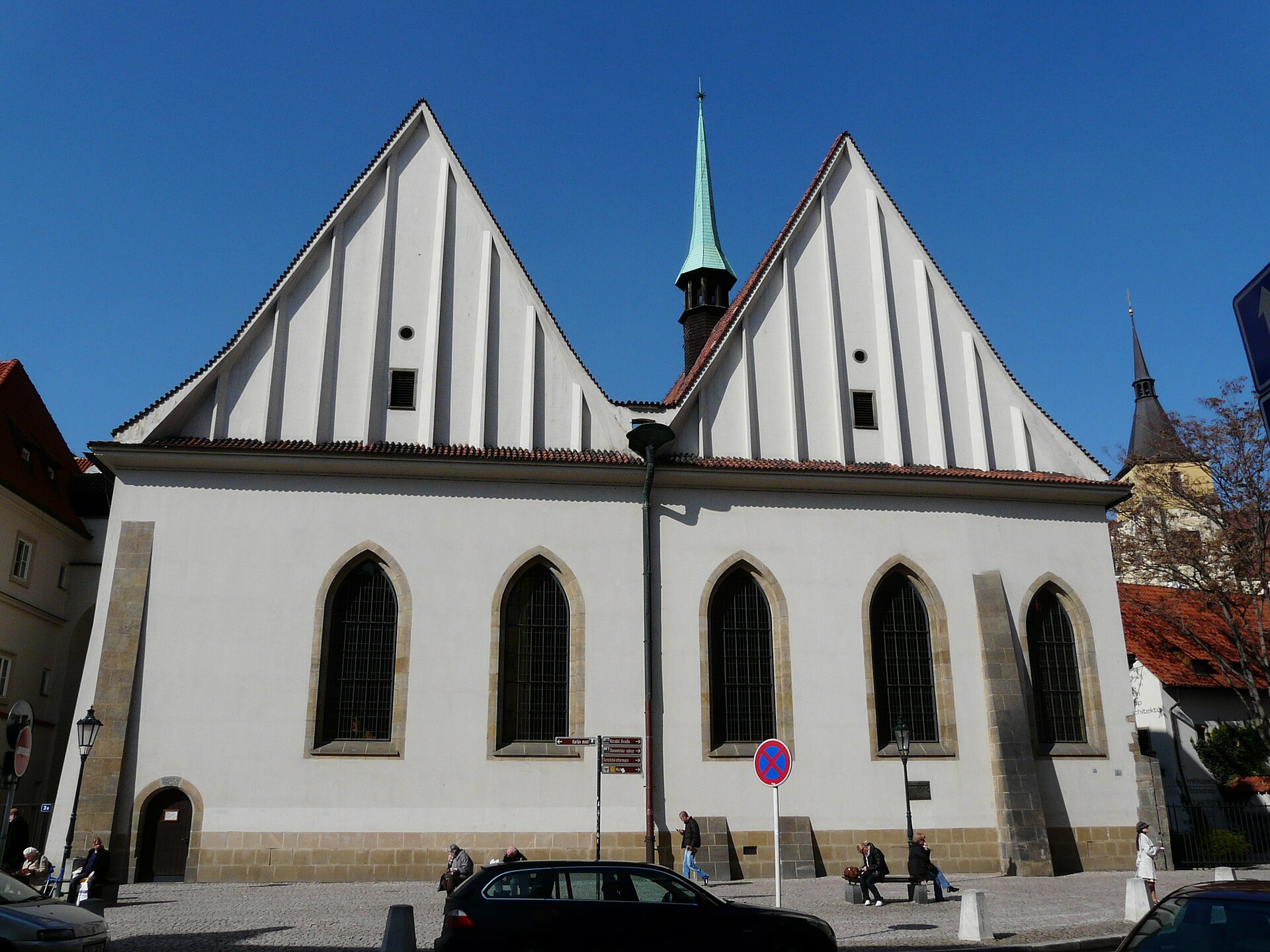 The front of a large white building with a pair of tall steep gables and a row of plain windows on a city street