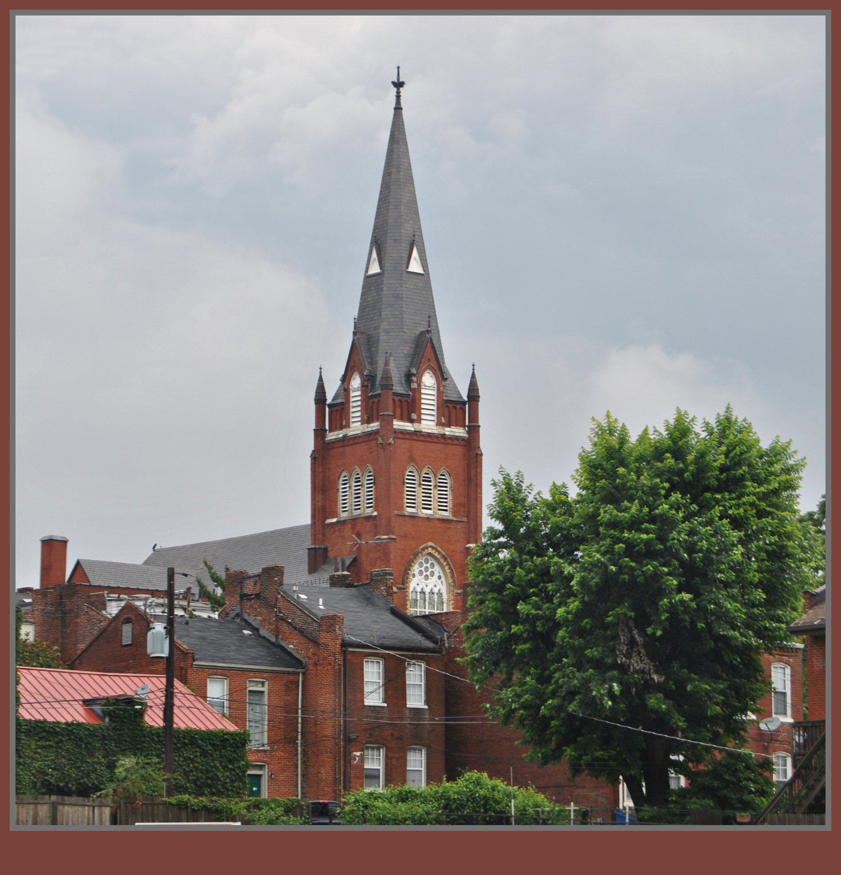 Red brick Gothic Revival church with a tall central spire on a city street