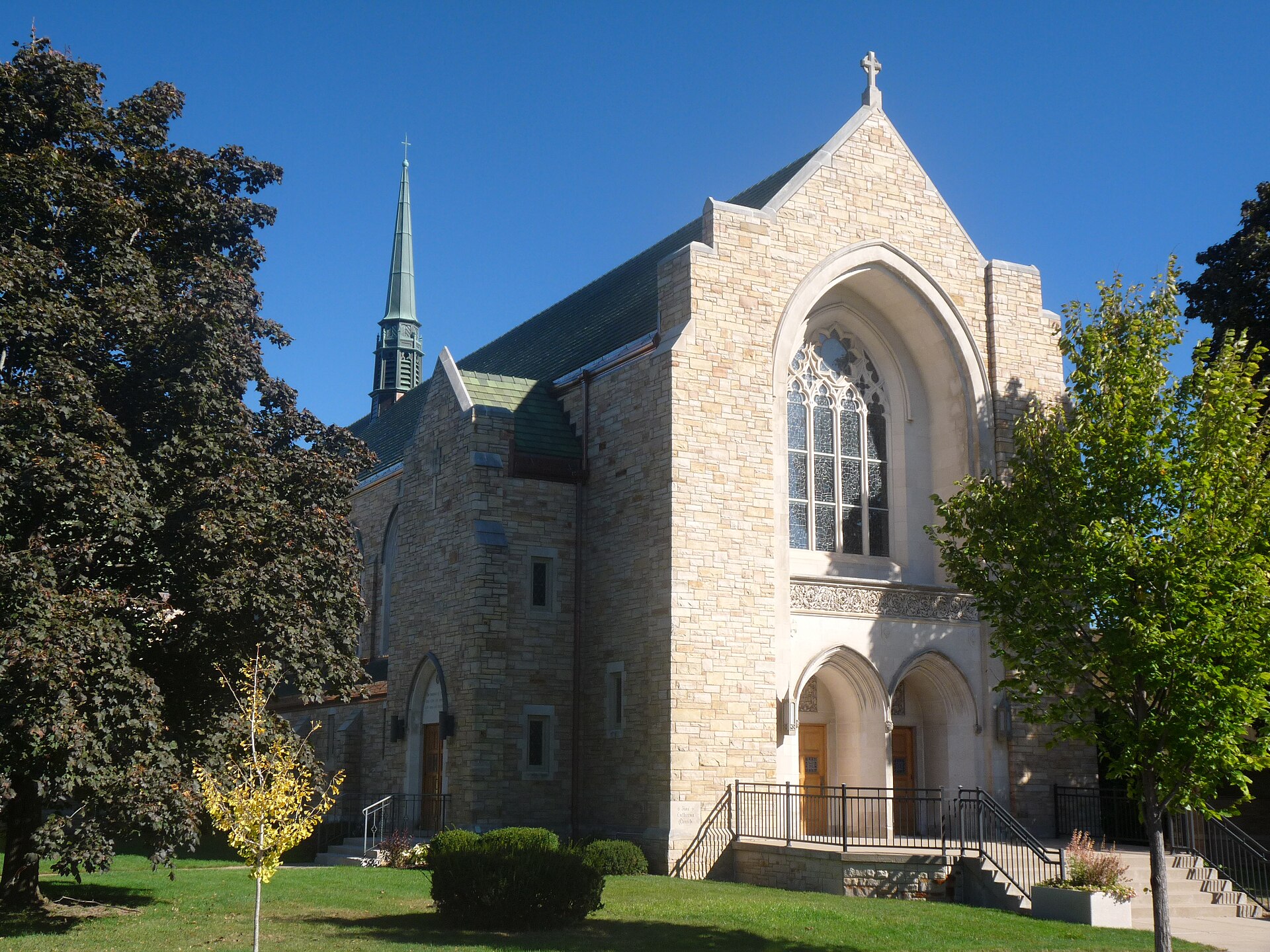 Stone Gothic Revival church with a square bell tower and pointed arched windows beside a street
