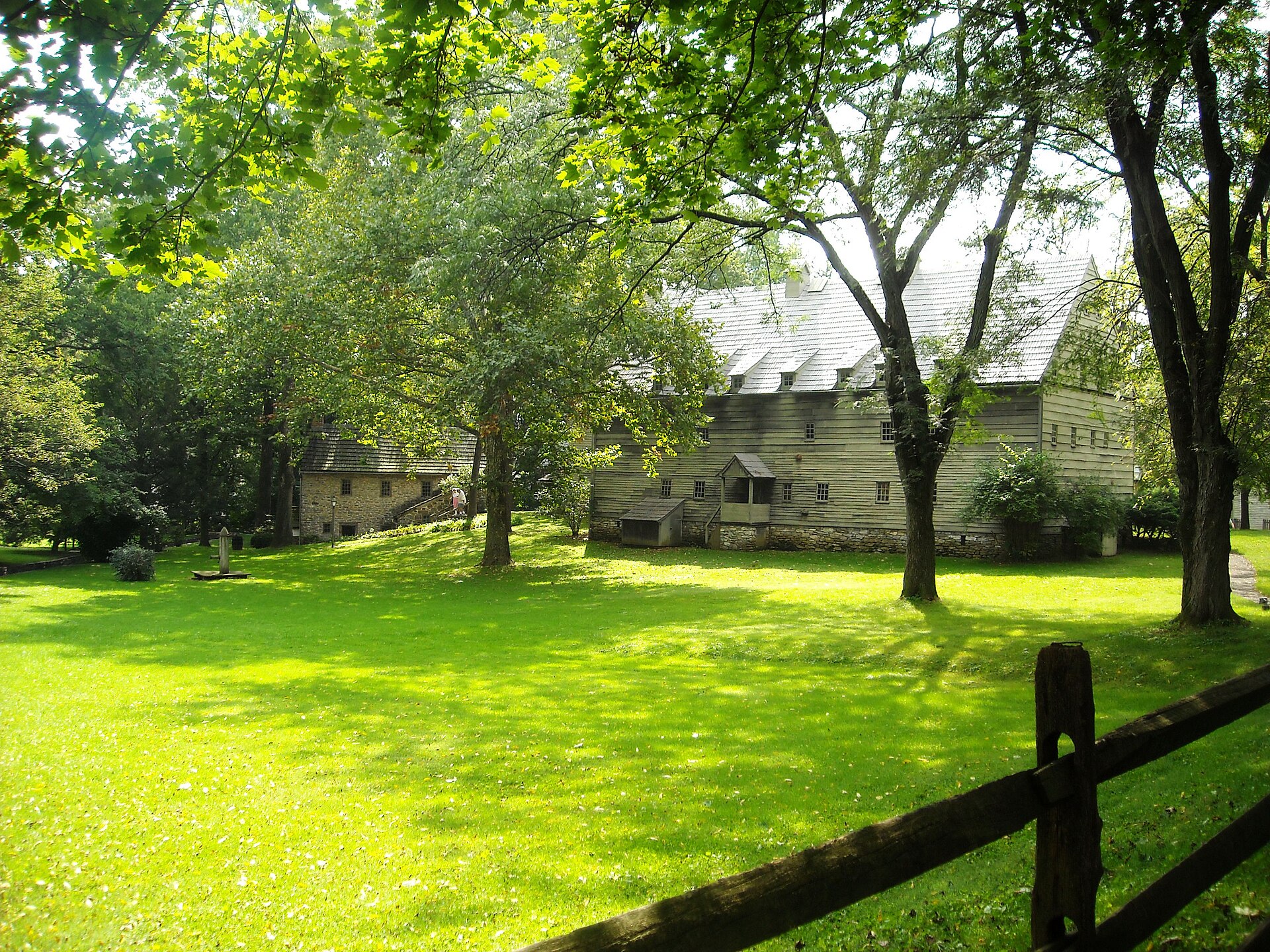 Tall steep-roofed wooden and stone buildings with many small windows standing on a grassy slope