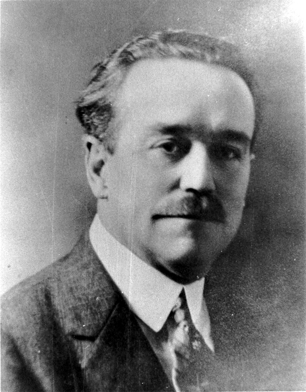 Black and white studio portrait of Charles Fox Parham, a clean-shaven man with a mustache, in a dark suit with a high collar