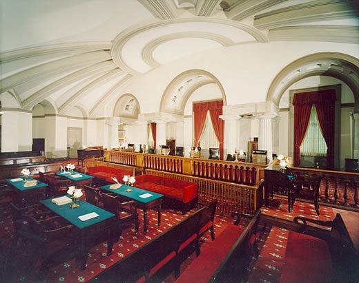 A semicircular vaulted room with a raised bench, a row of chairs and a low railing