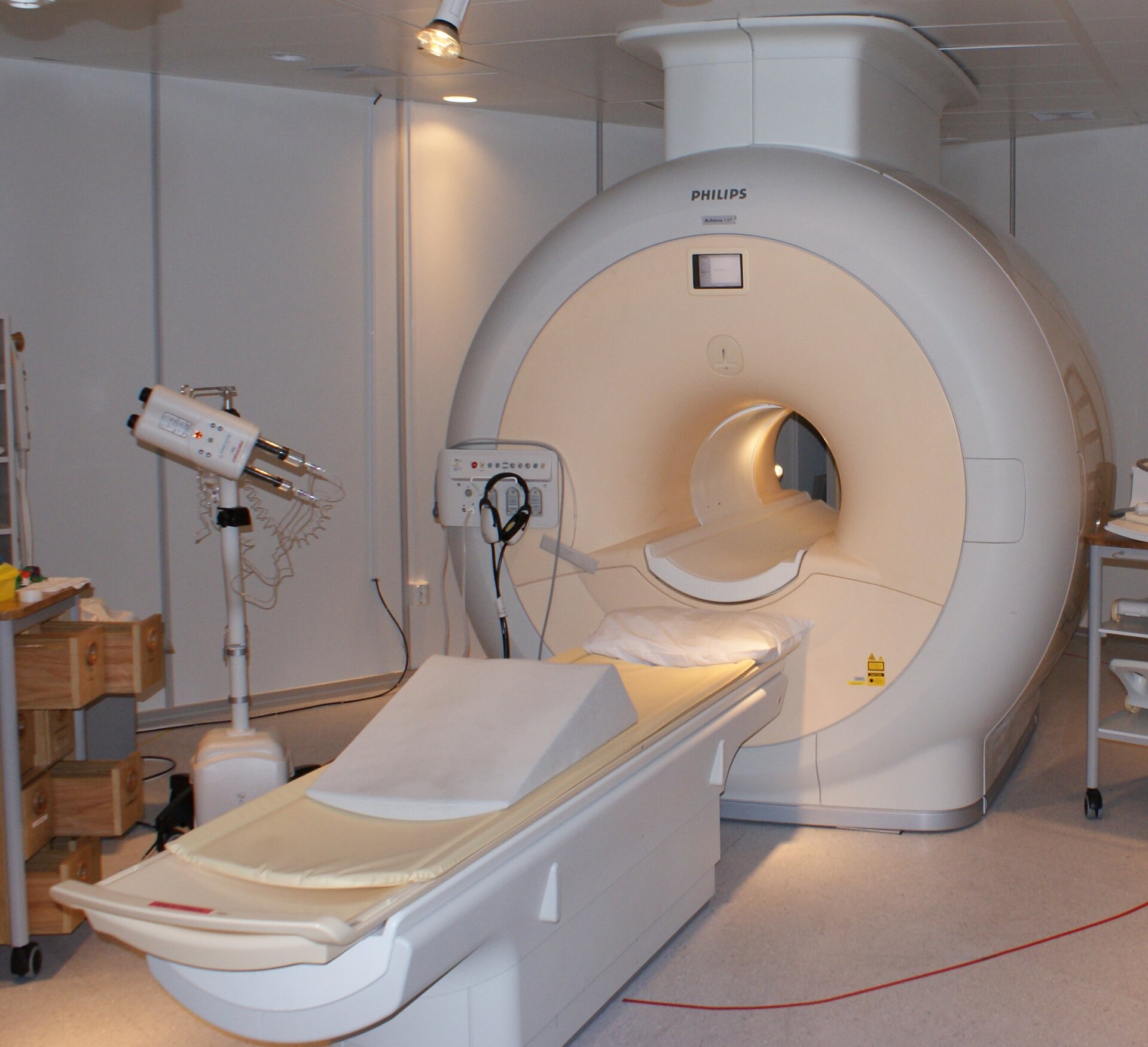 A large white MRI scanner with a circular opening and a padded patient table extending from it, in a clinical room