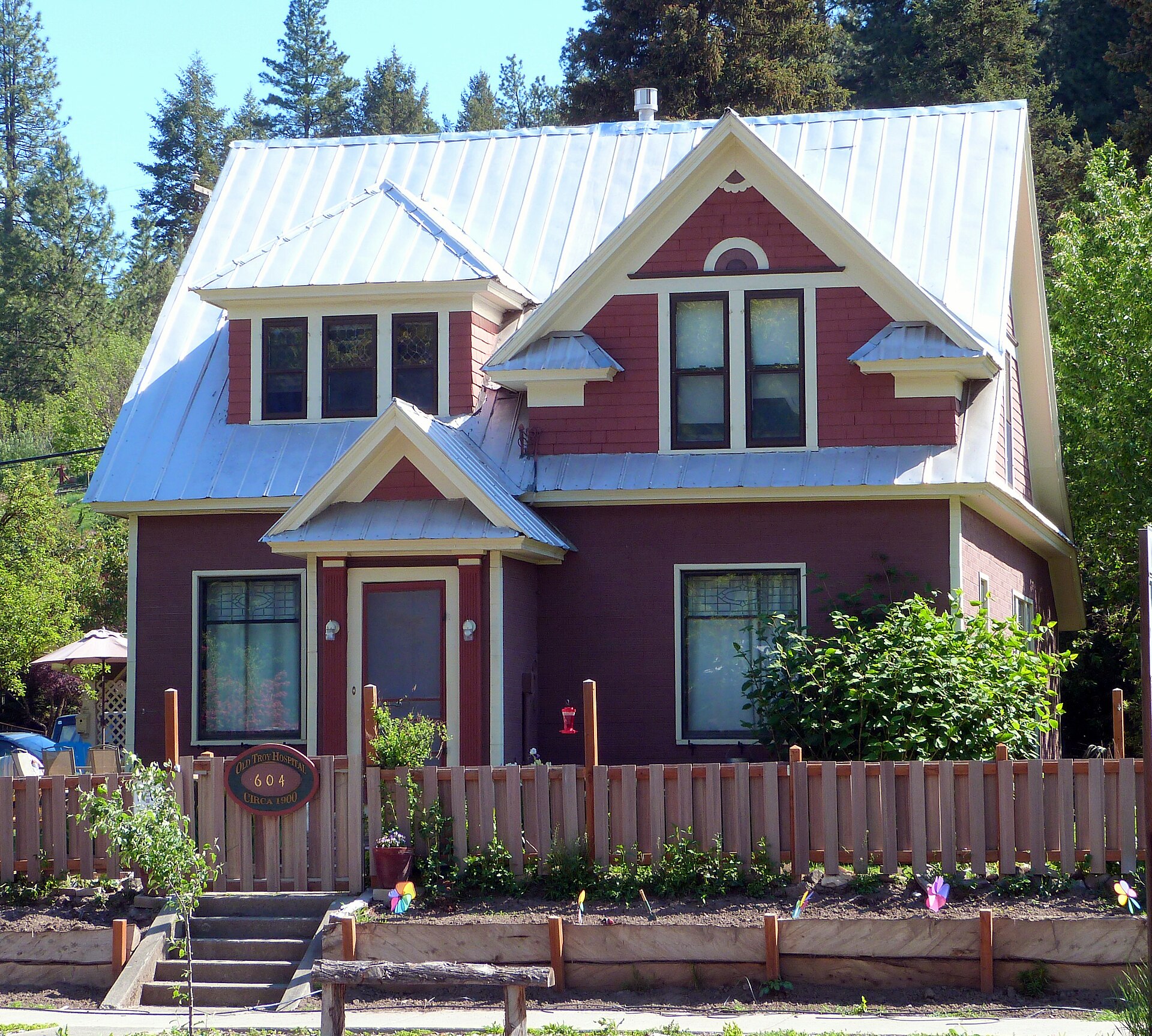 A two story red brick building with white trim and a front porch on a small town street, the historic Troy Hospital in Troy, Idaho.