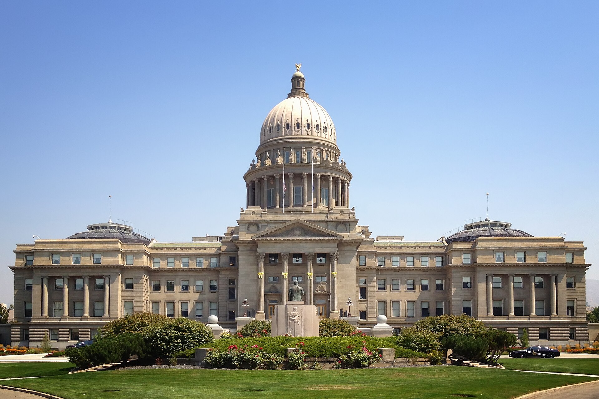 The Idaho State Capitol in Boise, a white neoclassical building with a large central dome and columned front, under a blue sky.