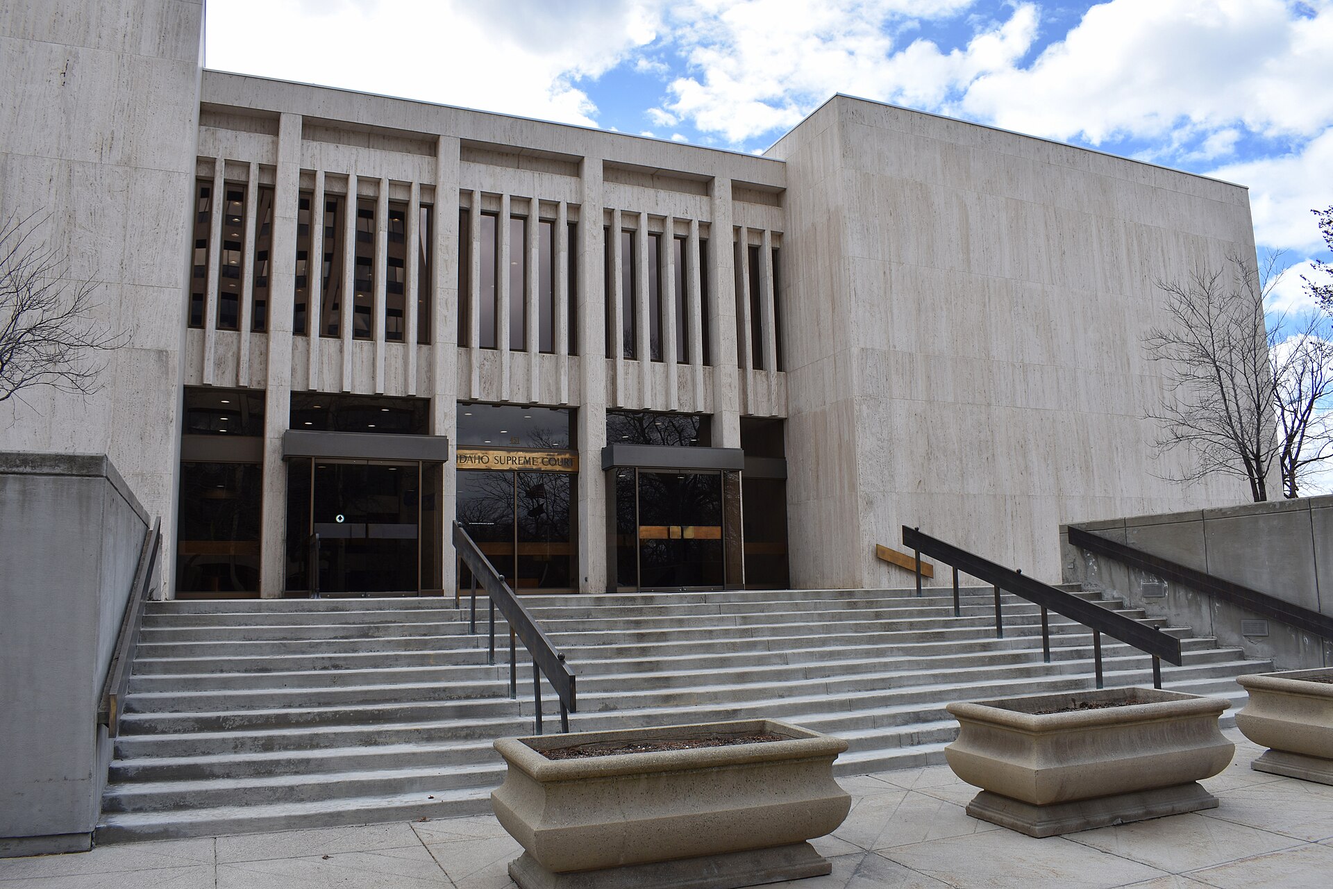 The Idaho Supreme Court building in Boise, a low modern stone building with tall vertical windows, seen from the street on a clear day.