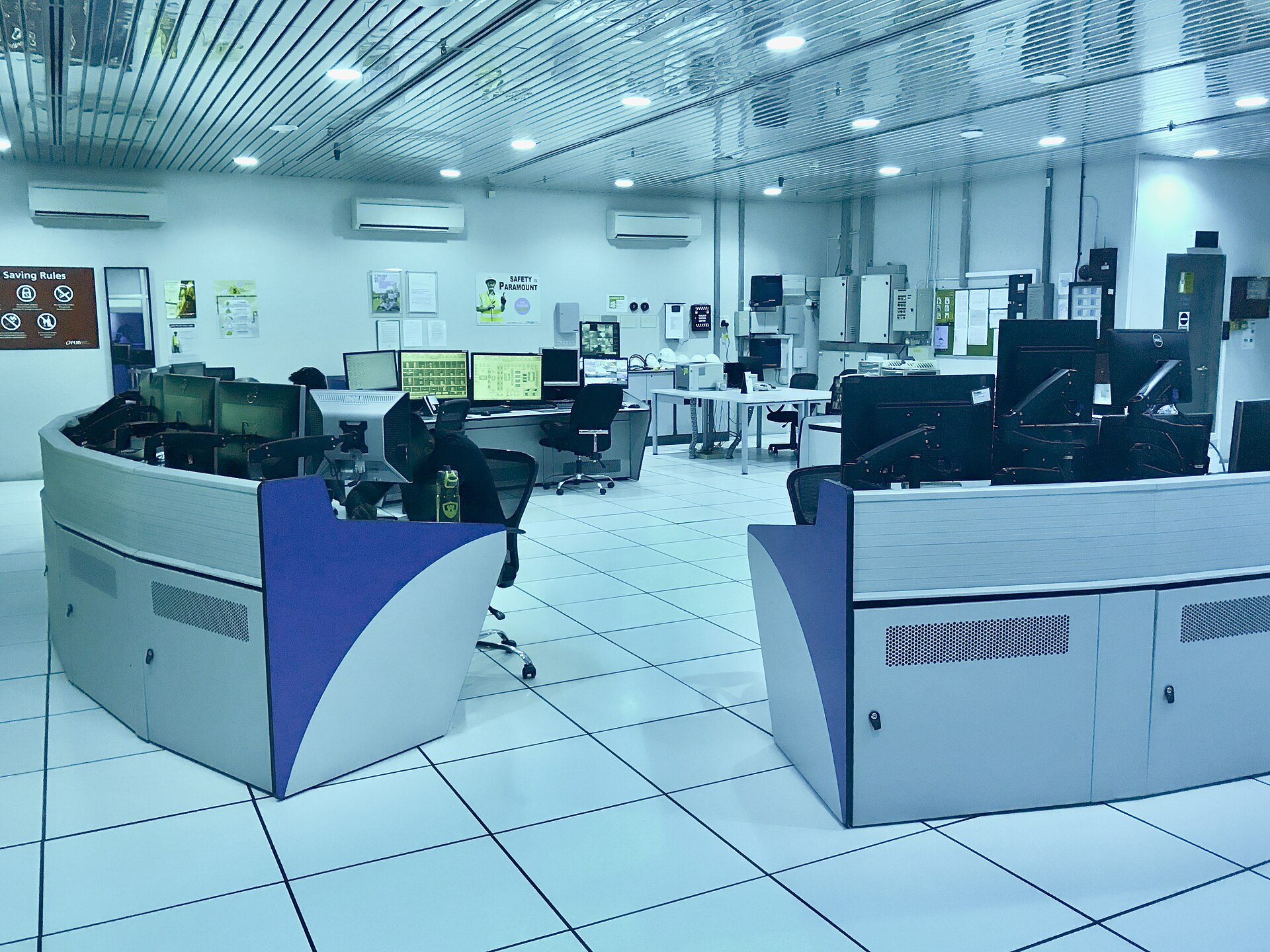 A control room with a wall of large screens showing process diagrams and rows of operator desks with computer monitors, at a water plant.