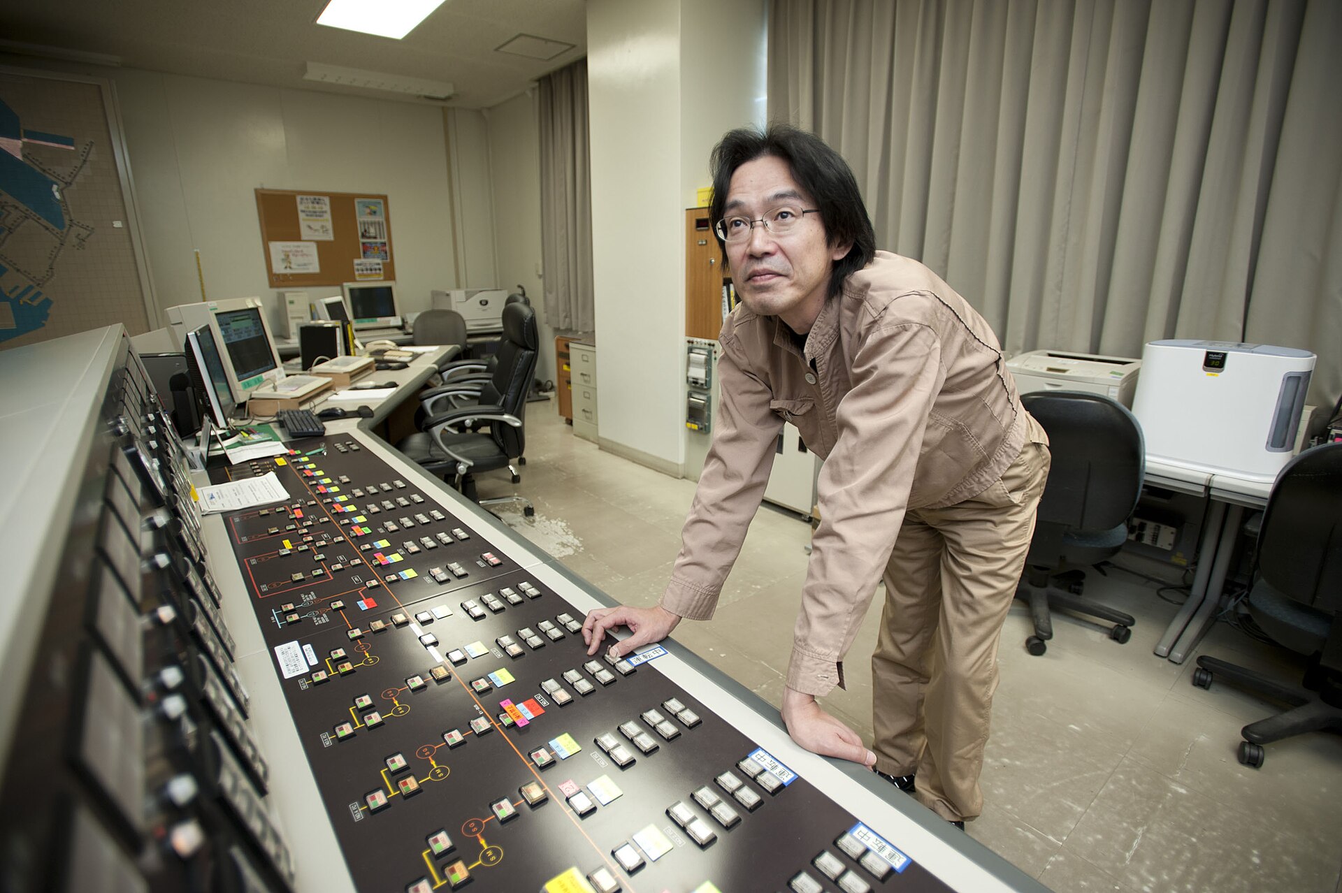 A man seated at a desk with several computer monitors showing an electrical system diagram, operating a SCADA system in a control room.
