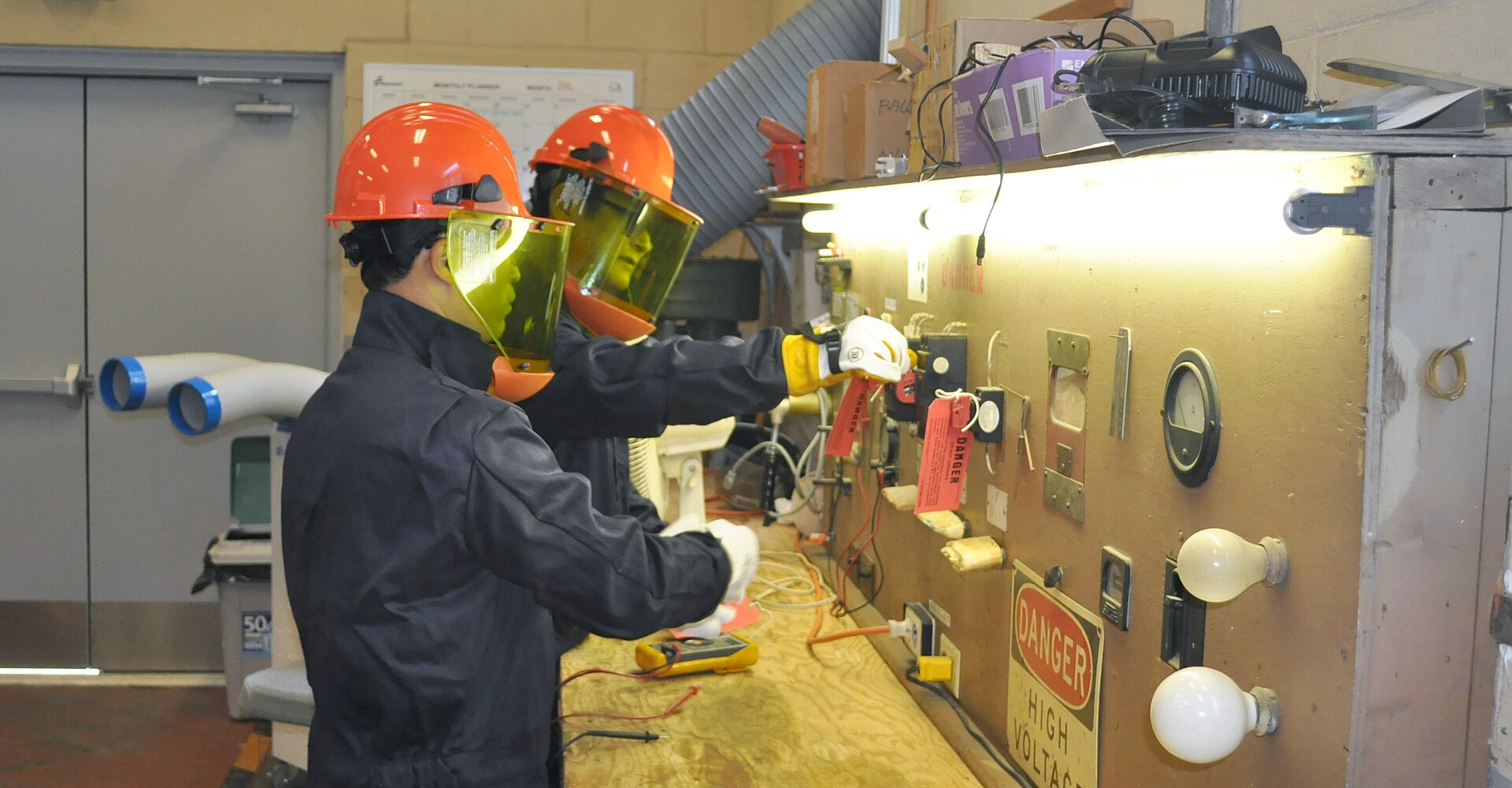 Two men in work clothes stand at a table in a meeting room reviewing printed lockout and tagout procedure documents together.