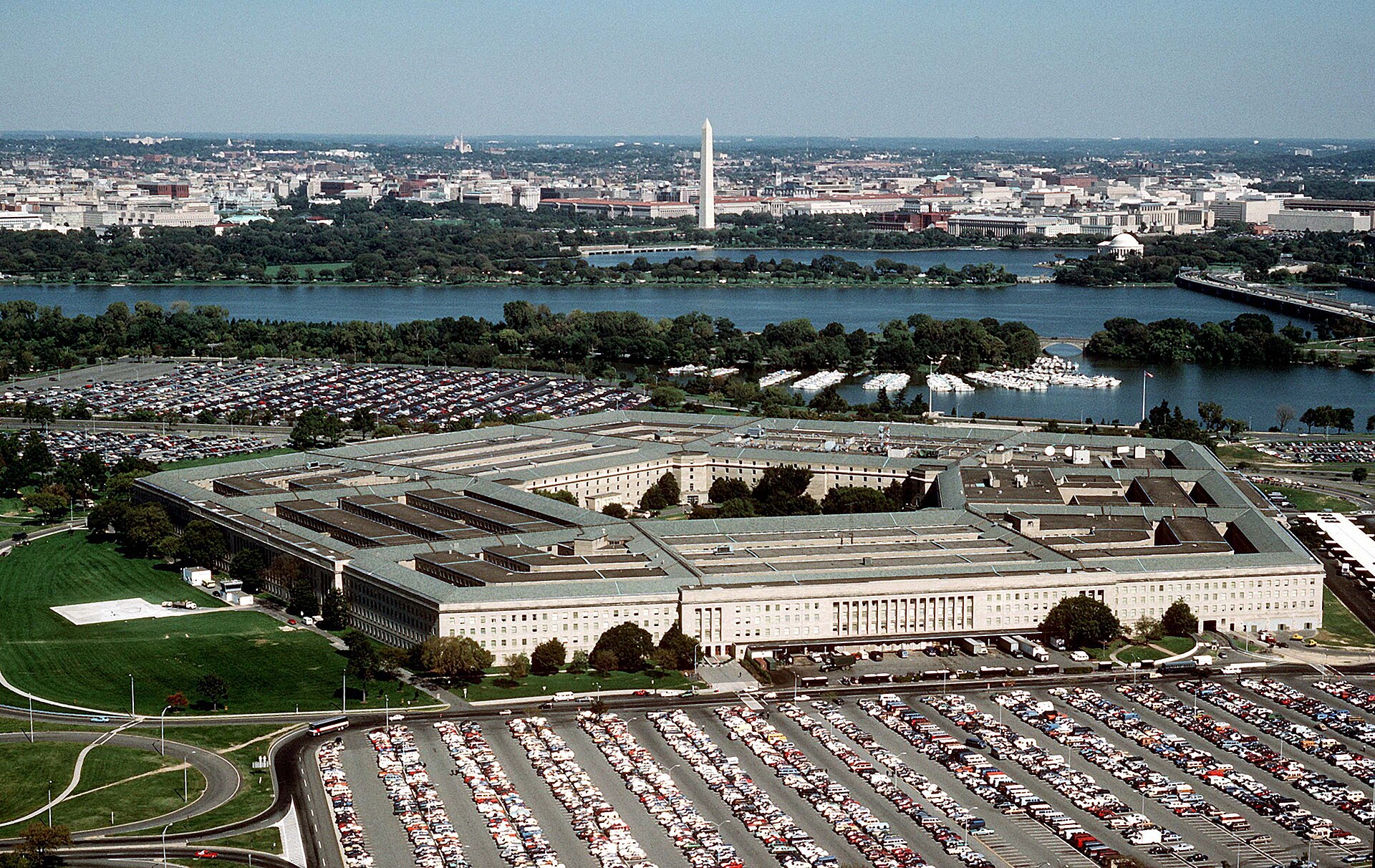 Aerial view of the five-sided Pentagon building, with the Potomac River and the Washington Monument visible in the distance.