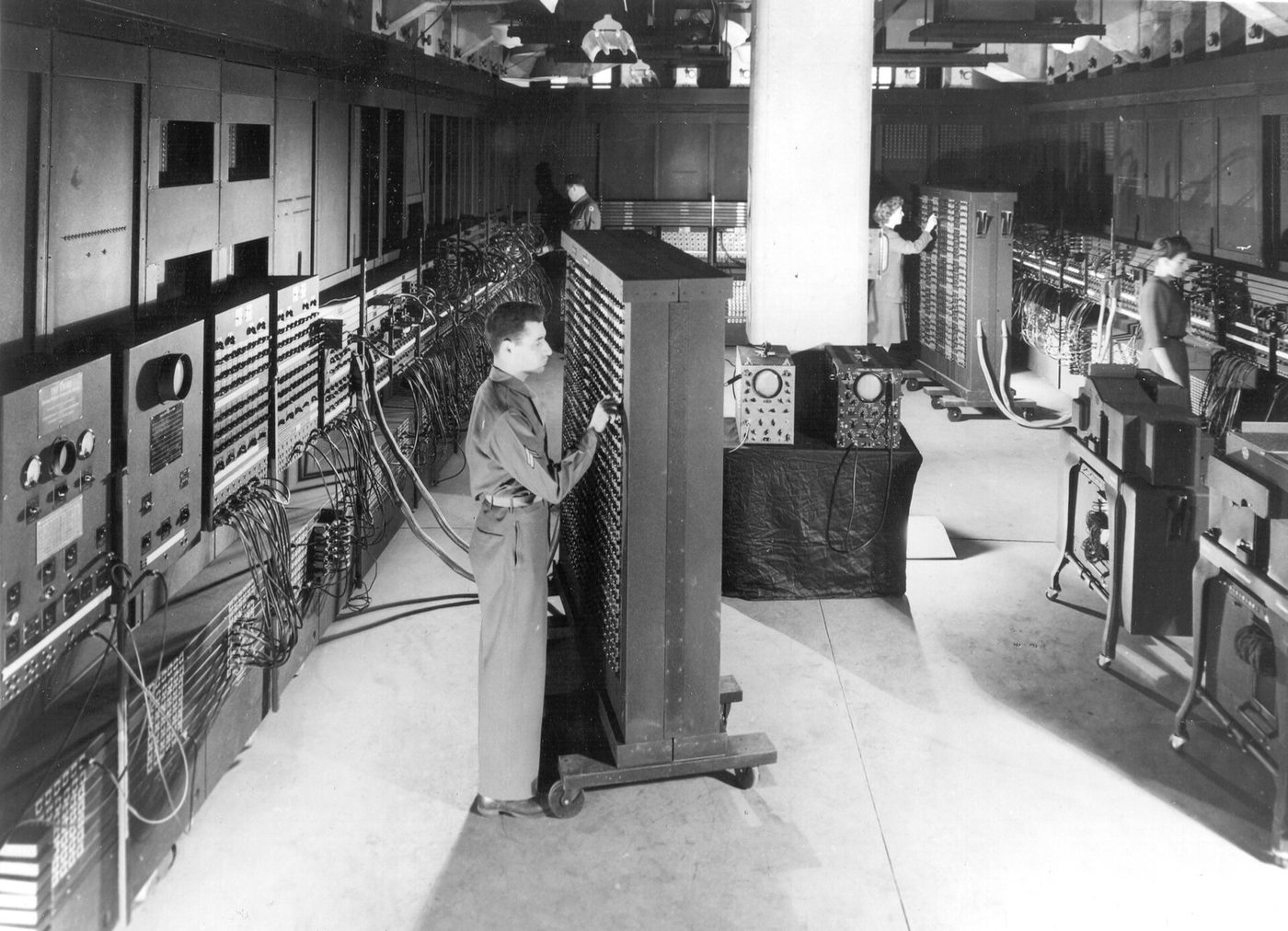 A uniformed soldier sets switches on a tall panel of the ENIAC computer