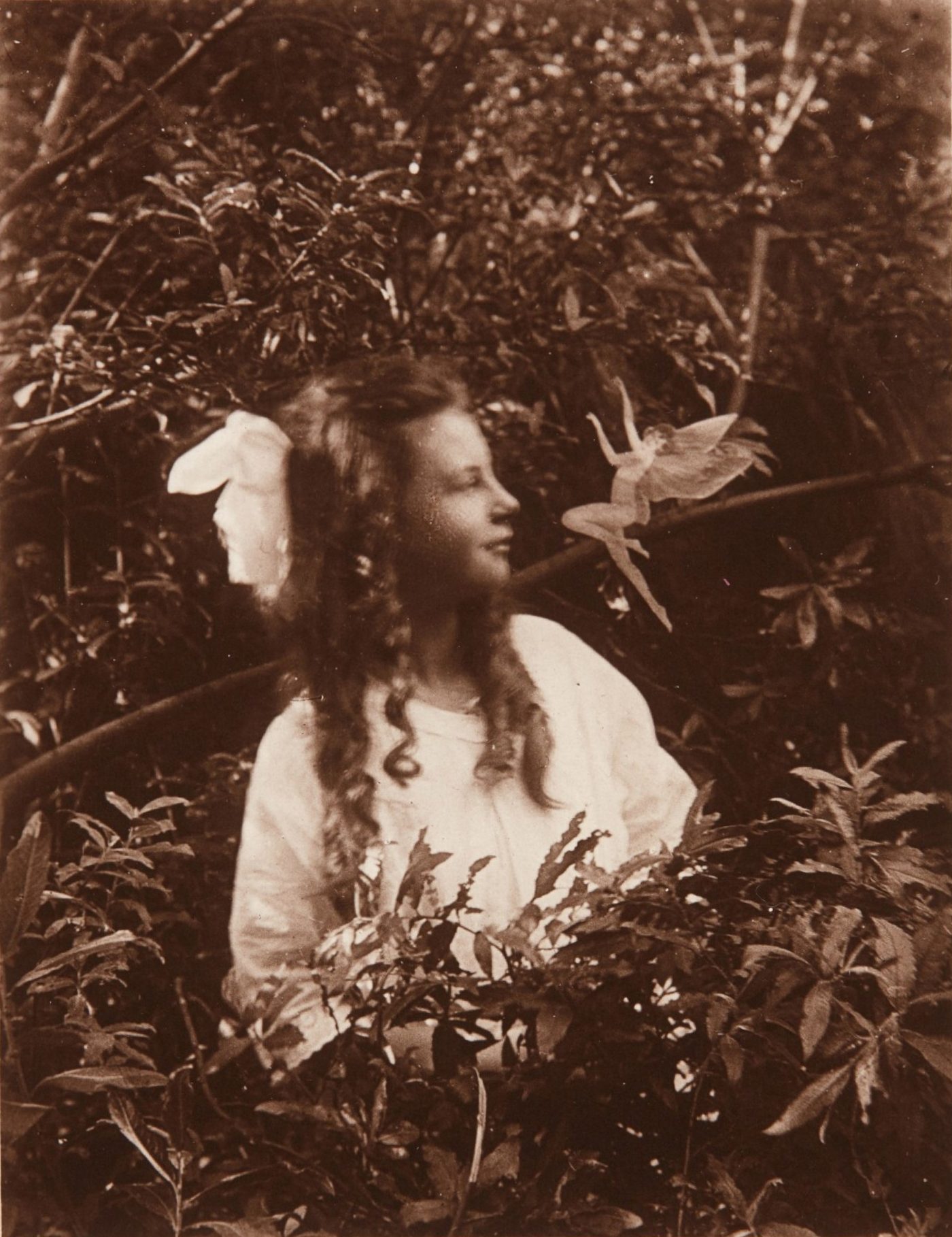 A girl looks toward a small winged figure in the air beside her face, in an old sepia photograph