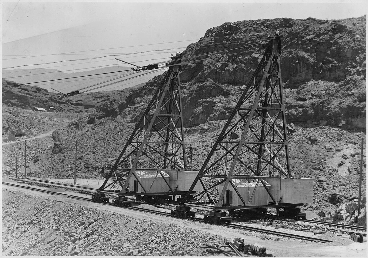 Black-and-white photograph of workmen on a skip suspended from a cableway at the Hoover Dam construction site