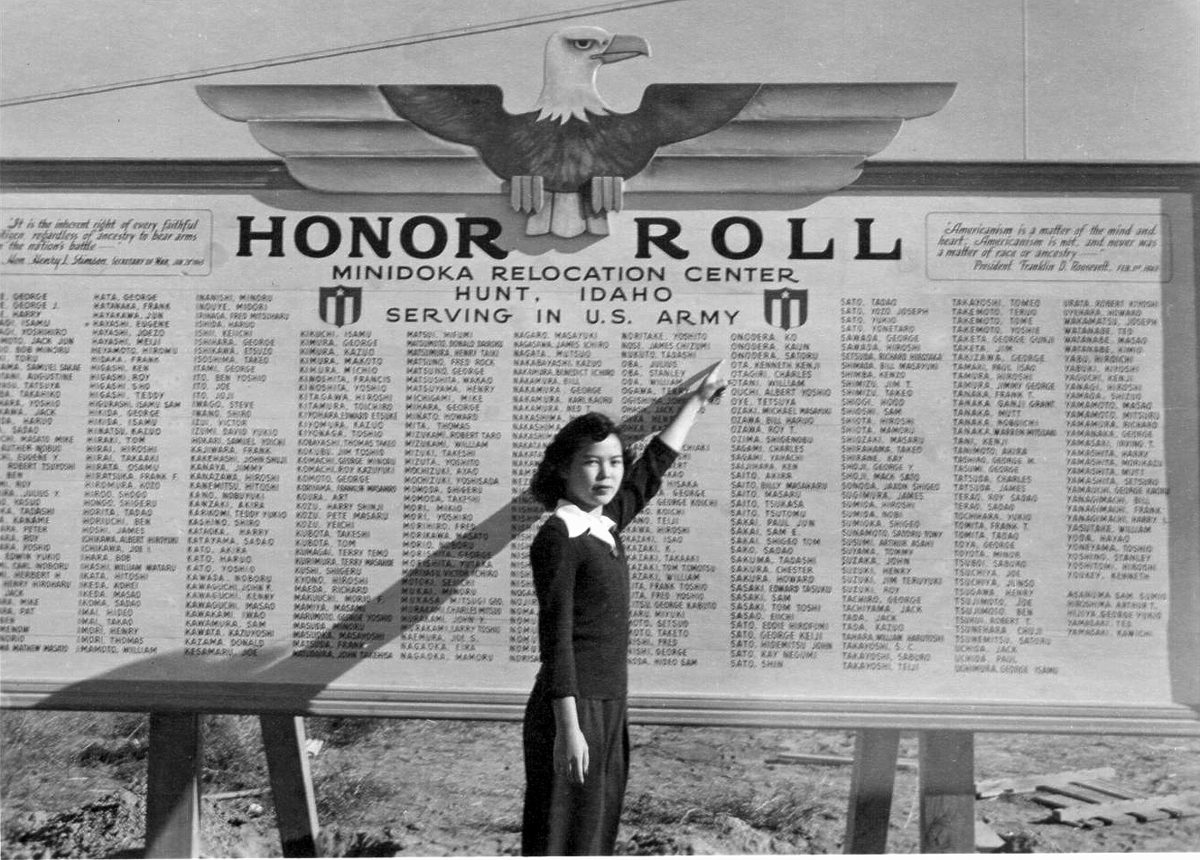 Black and white photograph of a large three-panel signboard topped by an eagle reading HONOR ROLL, Minidoka Relocation Center, Hunt, Idaho, Serving in U.S. Army, with columns of names