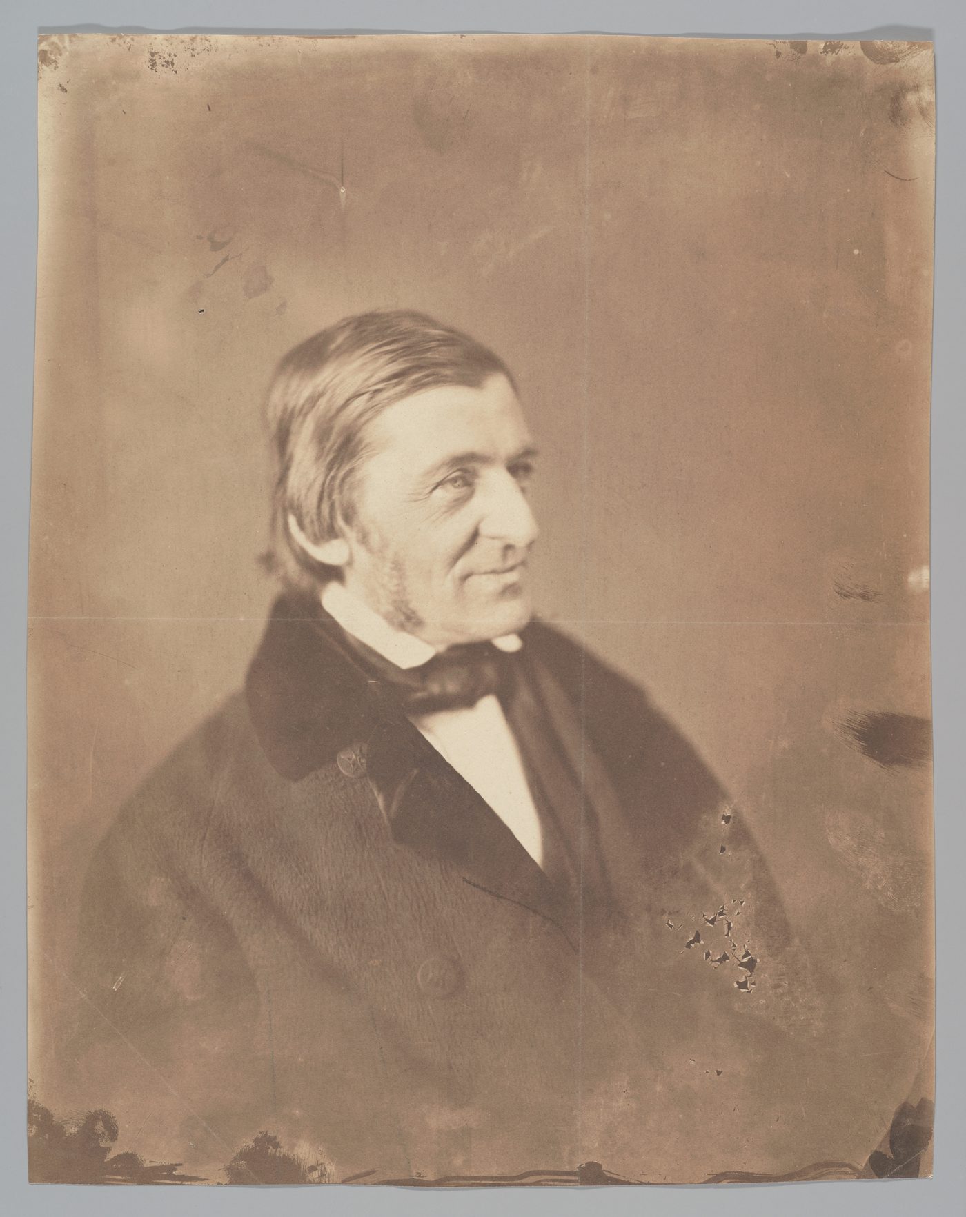 A photograph of Ralph Waldo Emerson in middle age, seated, in a dark coat, looking to the side with a long, thin face