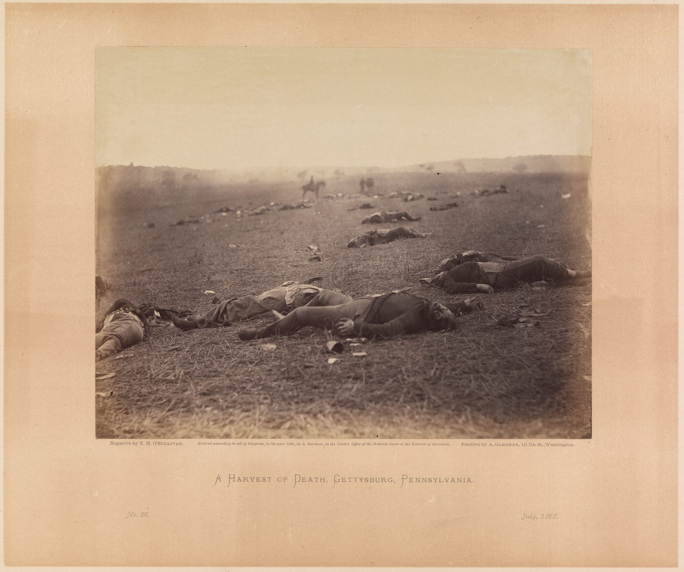 A photograph of dead soldiers lying scattered across a field at Gettysburg, shoes pulled off, with a man on horseback faint in the mist behind