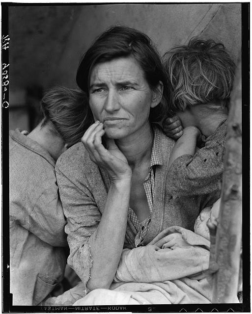 A woman in a worn jacket looks past the camera with her hand at her chin while two children lean their faces against her shoulders and an infant lies in her lap.