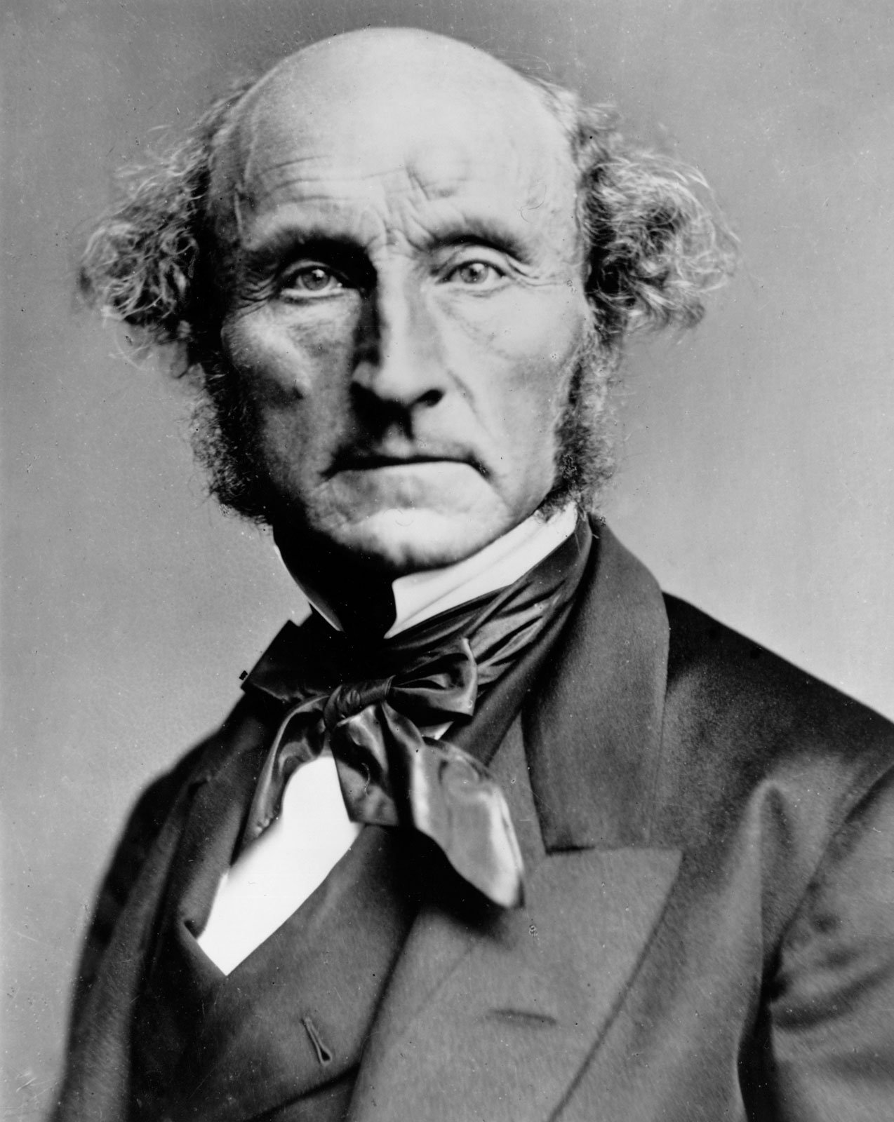Black and white photograph of John Stuart Mill, a balding older man in a dark frock coat, seated and looking to one side