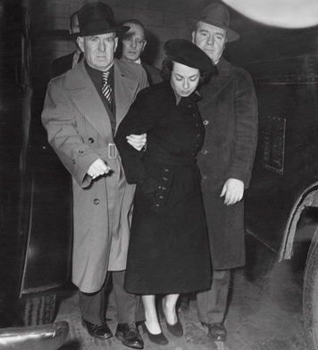 Black and white news photograph of Judith Coplon being escorted by FBI agents at the time of her arrest