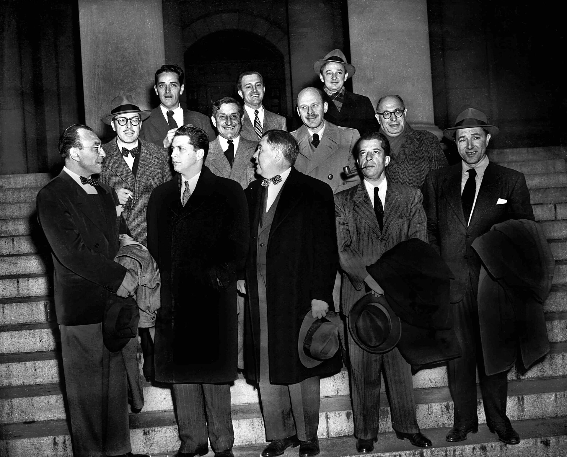 A group of men in suits and overcoats standing together outside a courthouse building