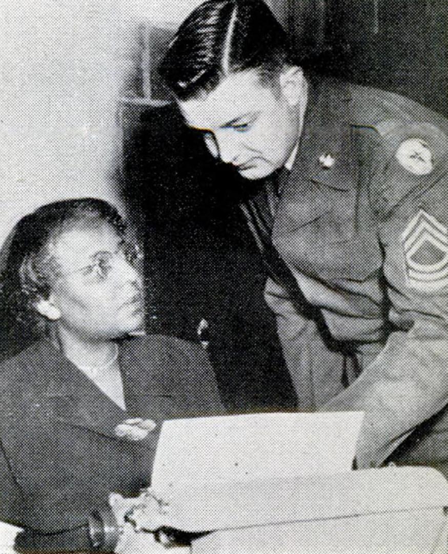 Annie Lee Moss, a woman in glasses seated at a desk with papers, looks up at a uniformed Army sergeant who leans over to speak with her