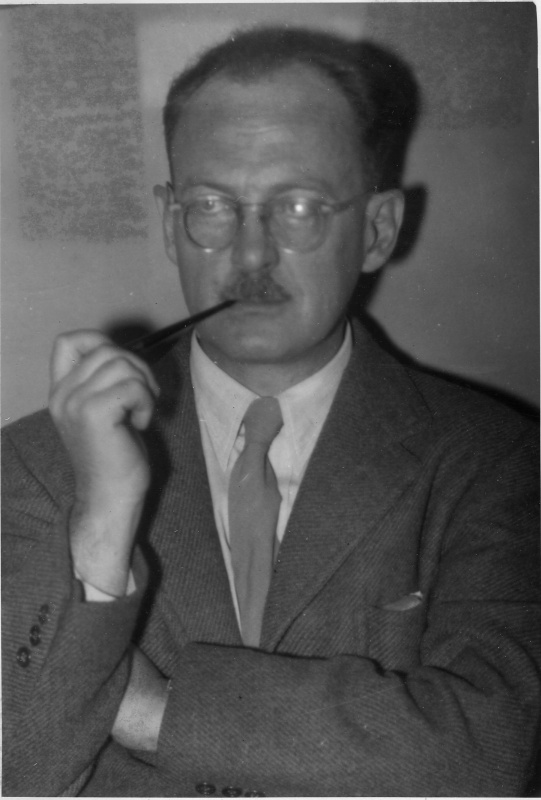 Black and white portrait of Owen Lattimore, a man with glasses and a moustache, holding a pipe to his mouth with his arms folded