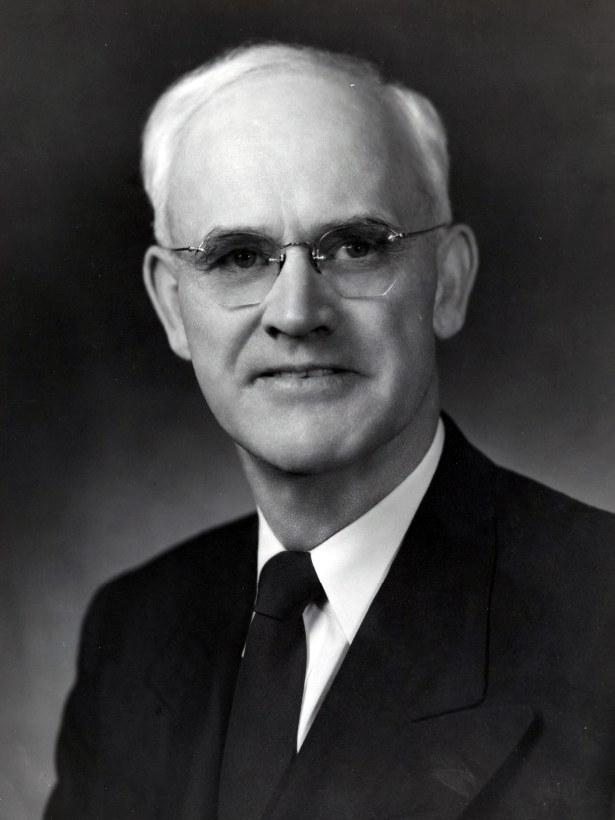 Black and white portrait of Arthur V. Watkins, a white-haired man with rimless glasses, wearing a dark suit, white shirt and dark tie