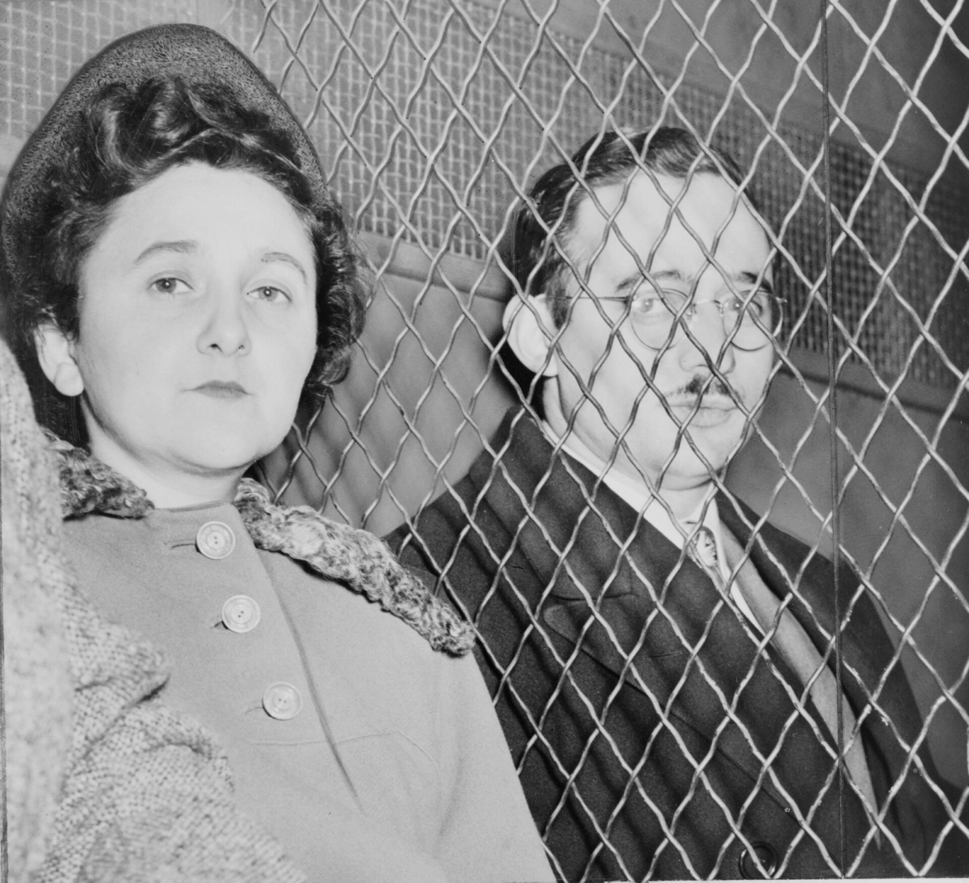 Julius and Ethel Rosenberg seated in the back of a van, separated by a heavy wire mesh screen, after their conviction