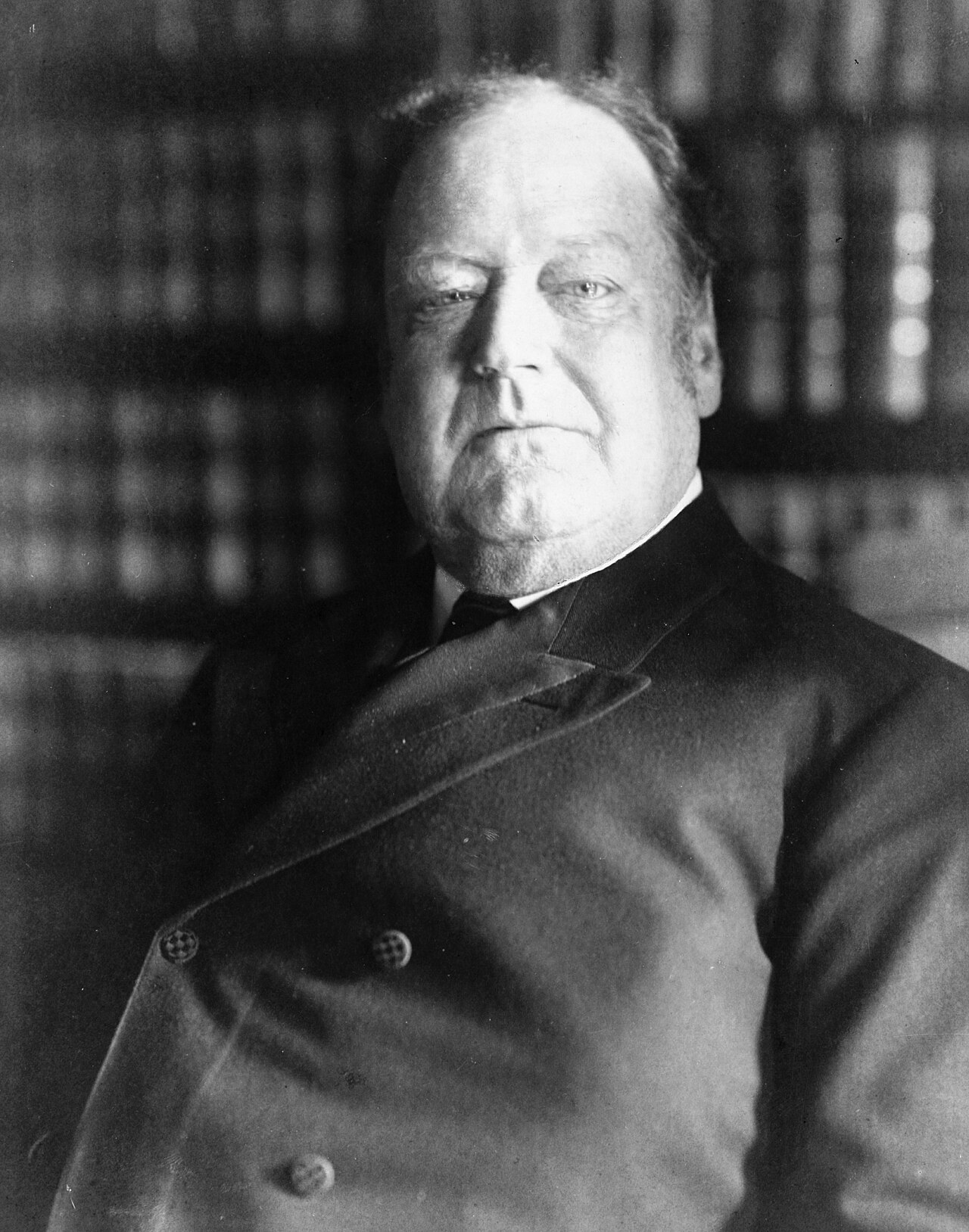 Black and white photograph of a heavy-set older man with a mustache in a dark suit, facing slightly left