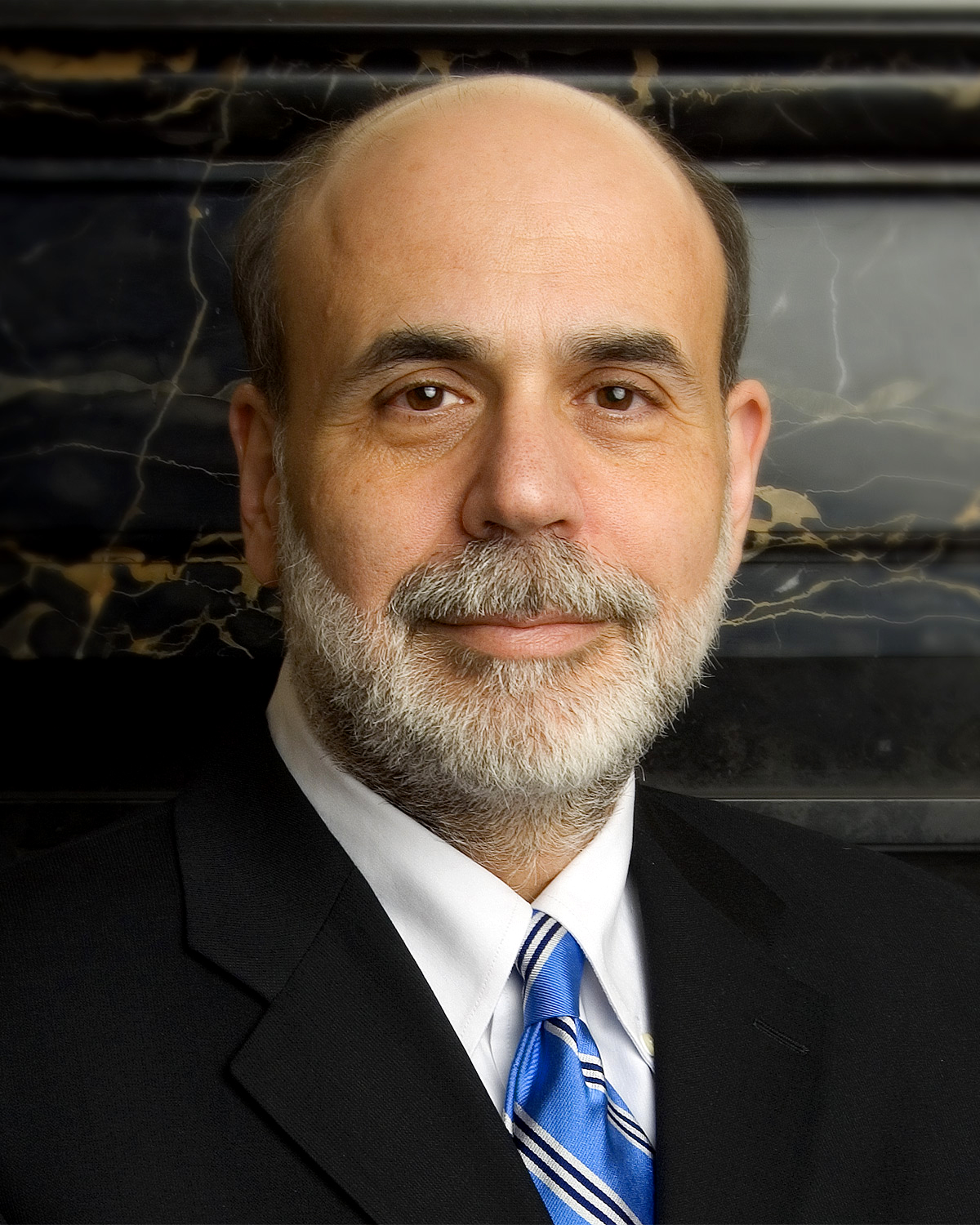 Formal portrait of Ben Bernanke, a bearded man in a dark suit and tie, in front of a flag