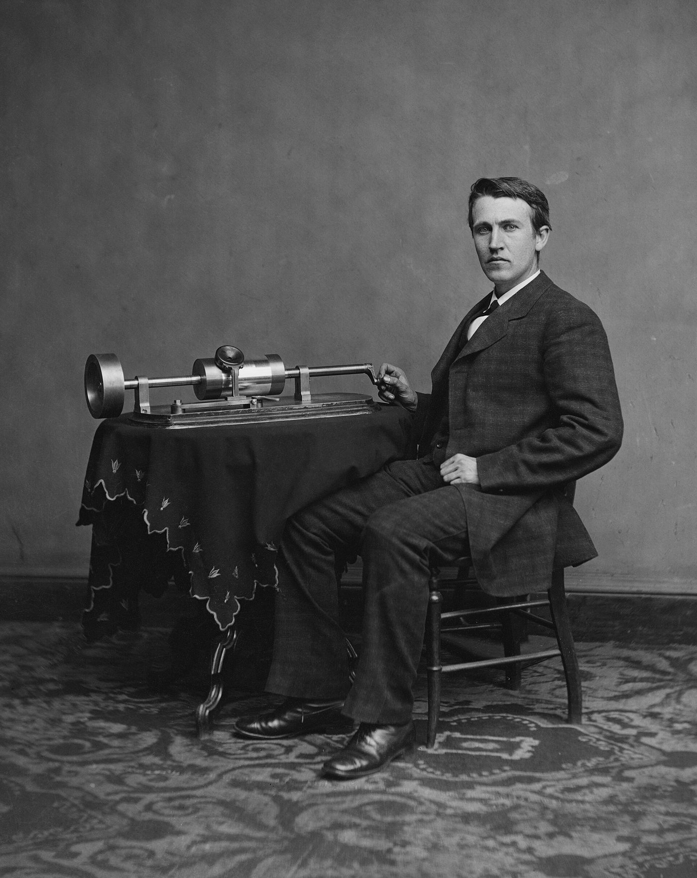 Thomas Edison seated beside his early tinfoil phonograph